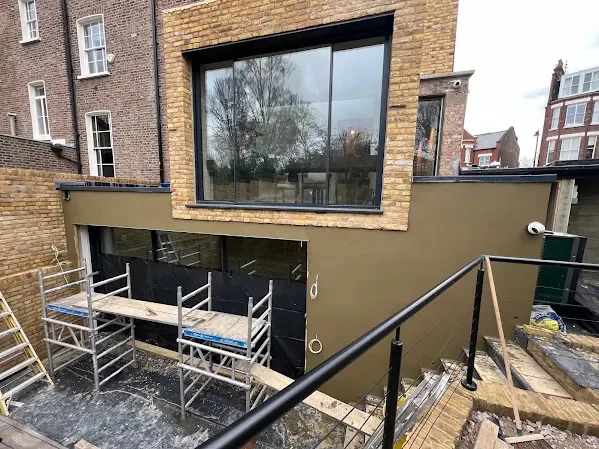 Modern block rendered dark around a full-height window, scaffold still up
