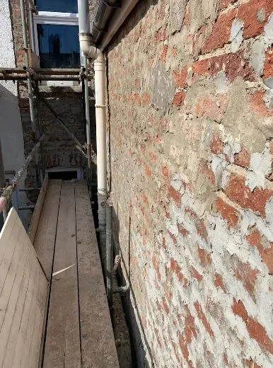 Before: an external wall hacked back to bare brick ready for a new render